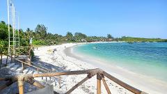 A breathtaking view of a white sandy beach with turquoise water, framed by a rustic wooden railing and lush green vegetation under a clear blue sky.