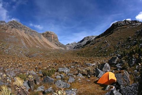 Sierra Nevada Cultural Immersion Experience (4 Days / 3 Nights) An orange tent sits nestled amongst rocks and vegetation in a vast mountain valley under a bright blue sky.