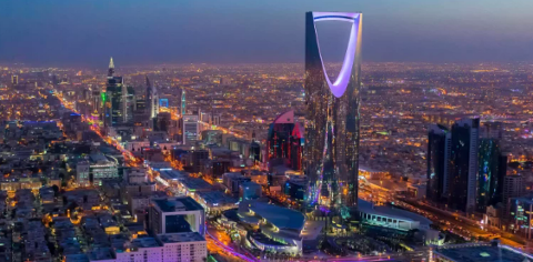 An aerial view of Riyadh, Saudi Arabia, showcasing the illuminated cityscape at night, dominated by the towering Kingdom Centre.
