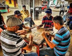 Darien Gap, Rainforest, and Culture from Panama Four older men are sitting around a wooden table outdoors, playing dominoes, with two other older men watching nearby.