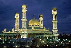 This is a nighttime view of the Sultan Omar Ali Saifuddien Mosque in Brunei, featuring its golden dome and minarets illuminated against a dark blue sky.