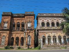 Two old, ornate brick buildings stand side-by-side under a bright blue sky, showing their age and architectural details.