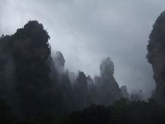 Misty, jagged rock formations rise dramatically under a heavy, overcast sky.