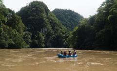 A group of people are rafting on a river through a lush, green landscape.
