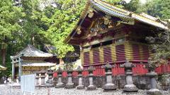 A colorful Japanese temple building stands surrounded by trees and stone lanterns.