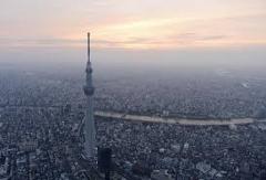 A tall tower, likely the Tokyo Skytree, rises above a dense cityscape under a hazy, pastel-colored sky.