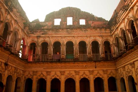 3-Day Dhaka Heritage & Culture Tour — Old Palaces, Lost Cities & Zamindari Mansions An ancient, ruined courtyard building with ornate arches, columns, and decorative carvings stands under a bright sky, hinting at a rich past.