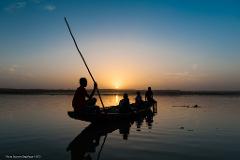 Silhouette of a boat with people on a calm lake at sunset.
