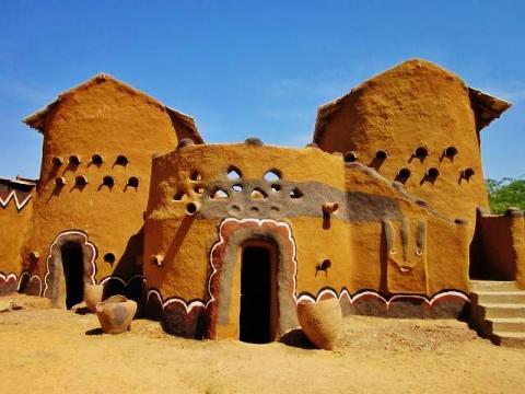 This image shows traditional earthen houses in a rural setting, featuring unique architectural designs with decorative elements and a clear blue sky.