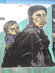 A mural depicting a woman carrying a child on her back, rendered in a stencil-like style with bold outlines and contrasting colors.