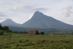 A scenic landscape featuring a small hut in a grassy field with two prominent mountains in the background under a cloudy sky.