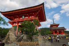 A vibrant red pagoda stands tall in Kyoto, Japan, with a stone lion and lush greenery adding to the scenic view, as tourists ascend the stairs.