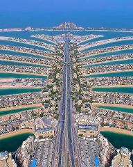 An aerial view showcases Dubai's Palm Jumeirah, a man-made archipelago with a central road leading to a large hotel at the end.