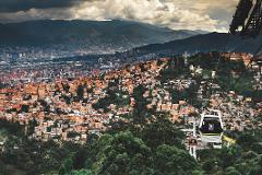 A cityscape of Medellín, Colombia with densely packed orange brick buildings climbing up the hillside and a cable car system in the foreground.