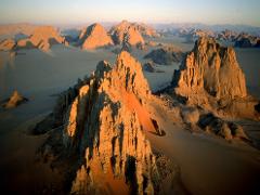 An aerial view captures striking rock formations bathed in golden sunlight, rising from a vast desert landscape.