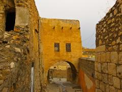An alleyway with stone walls and an archway leading to a street with old buildings, showcasing historical architecture.