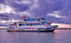 Here's a description of the image:A modern, two-story tourist boat with a white, purple, and blue design floats on calm water under a dramatic, cloudy sky.