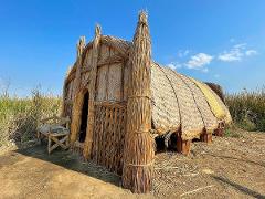 Une hutte unique, probablement faite de roseaux ou de paille, se dresse sous un ciel bleu vif à côté d&#39;une chaise en bois dans un champ d&#39;herbe sèche.