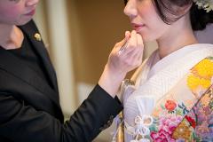 A makeup artist applies lipstick to a bride dressed in a traditional Japanese wedding kimono.