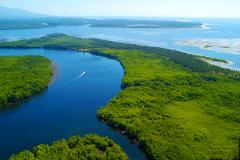 An aerial view of a tropical landscape with lush green islands, winding waterways, and a boat leaving a white trail in the blue water.