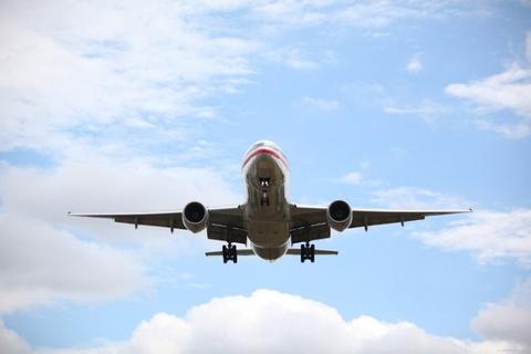 An American Airlines airplane is flying in the sky, with clouds in the background.