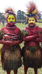 Ht Hagen, Witch Doctors, and Trekking Two people in traditional Papua New Guinean attire, complete with vibrant face paint, feathered headdresses, grass skirts, and red body paint, stand side-by-side in a field during a cultural festival.