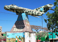 A military jet monument in Garowe, Somalia, commemorating the year 1988. The monument features a camouflage-painted aircraft atop a brick and painted base with illustrations.