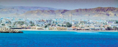 A vibrant coastal cityscape nestled between a blue sea and mountainous terrain.