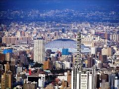 A dense cityscape with a large dome-shaped building in the midground and a tall communications tower in the foreground.