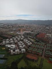 An aerial view of a sprawling city with diverse residential architecture, surrounded by distant mountains under an overcast sky.