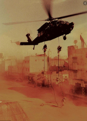 A Blackhawk helicopter hovers over a dusty urban landscape as soldiers descend on ropes toward the ground.