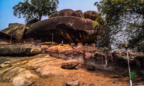 A large, dark rock formation dominates the landscape, with trees and structures surrounding it.