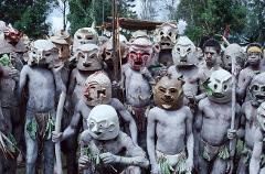 A group of men in Papua New Guinea, covered in light-colored paint and wearing elaborately decorated masks, are shown in a traditional gathering.