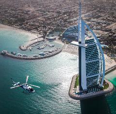 An aerial view shows a helicopter flying near the Burj Al Arab hotel, situated on an artificial island in Dubai, with a marina and cityscape visible in the background.
