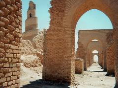 This shot captures the ancient architecture of Samarra, Iraq, highlighting a spiral minaret and arched walkways constructed from weathered brick.