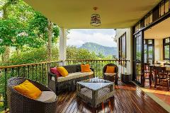 This outdoor patio features wicker furniture, a glass coffee table, and a view of a lush green landscape and mountains.