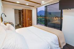 A cozy bedroom features a large bed with white linens and a tan throw, next to a sliding glass door offering a scenic mountain view and string lights.