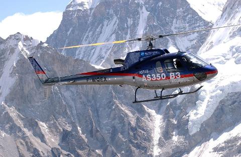 A helicopter flies amidst snow-capped mountains.