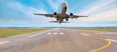 A plane takes off from a runway with a blue sky and clouds in the background.