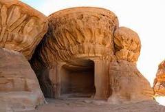 Here's a one-sentence description of the image:A rock formation featuring a large, rounded sandstone structure with a dark cave-like opening at its base, likely shaped by natural erosion.
