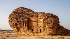 A rock formation in a desert landscape features carved facades with staircase designs and doorways.