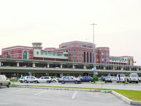 This image shows the Allama Iqbal International Airport building with multiple cars parked in front of it.