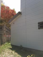 A side view of a white building with a sloped roof shows a red-leaved tree in the background and a red and white striped pole in the foreground.