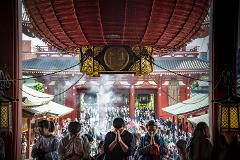 Through a temple's entrance, a crowd of praying people is seen, framed by the ornate lantern hanging above.