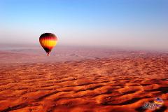 A hot air balloon floats over a vast, undulating desert landscape under a clear blue sky.
