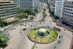 An aerial view of a bustling city intersection with a prominent roundabout featuring a lotus-shaped fountain in the center.