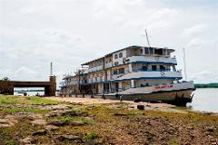 A large, multi-decked boat named "Tombouctou" is docked on a rocky shore, with a bridge and some figures visible in the background.