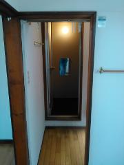 An open doorway reveals a small room with a mirror reflecting a person in blue clothing, with a bright light source visible in the background.