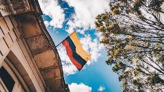 Excursión de un día al Patrimonio Cultural Zenú A Colombian flag waves proudly in front of a building and a tree under a blue sky with white clouds.