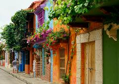 Excursión de un día al Patrimonio Cultural Zenú A colorful street scene shows vibrant colonial buildings adorned with flowers and greenery, while a couple strolls along the sidewalk.
